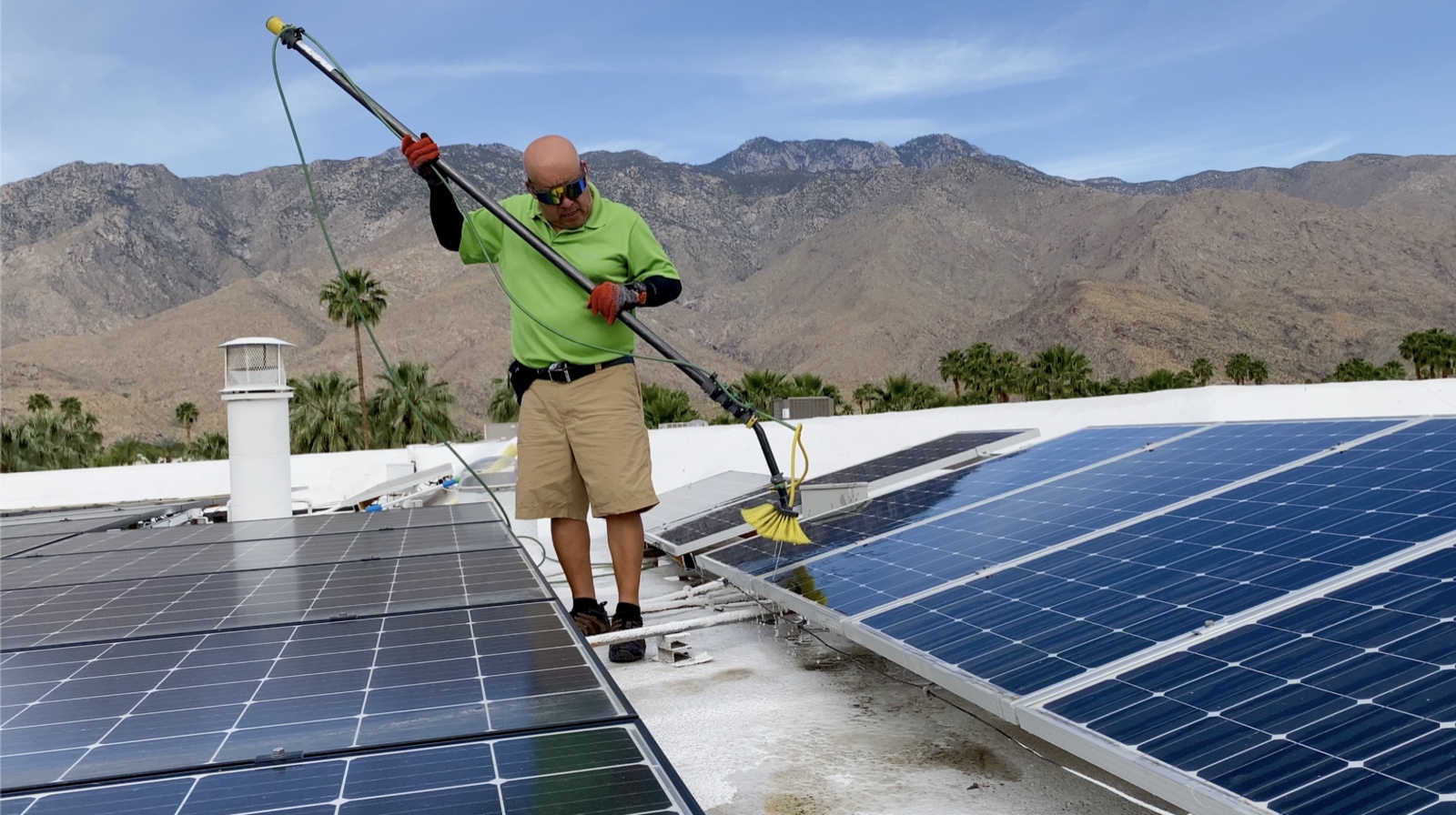 Lalo Rico cleaning solar panels on a Coachella Valley rooftop with the desert mountains in the background