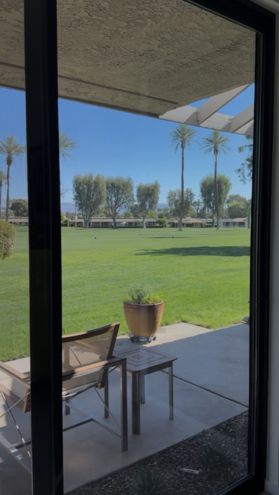 Same sliding glass door after cleaning — crystal clear, the palm trees and golf course view come through unobstructed